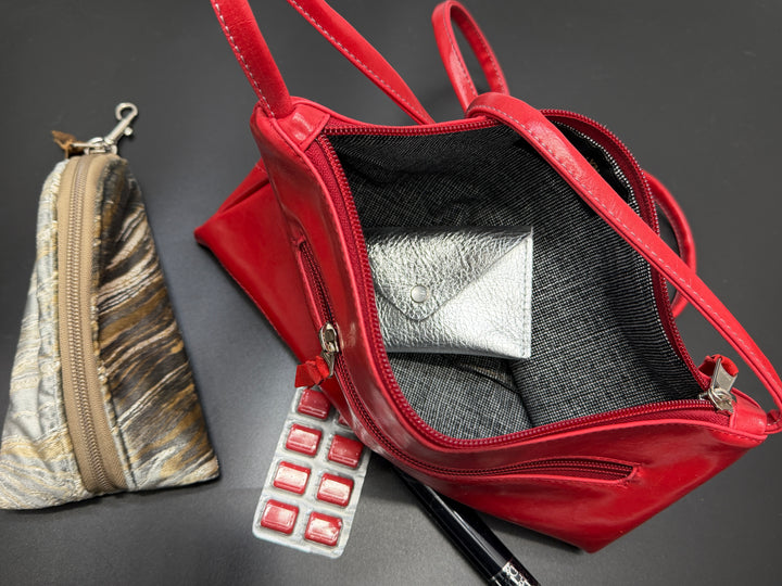 Red handbag with makeup items on a dark surface