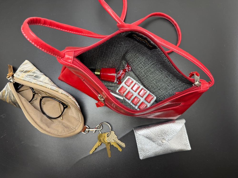 Red handbag with contents including a beige pouch, keys, and a silver wallet on a dark surface.