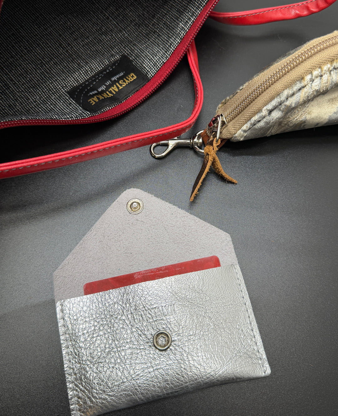 Close-up of a silver leather cardholder with a red interior on a gray surface.