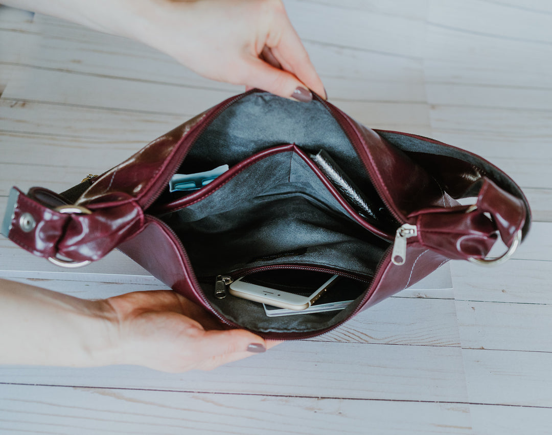 Open burgundy handbag on a light wooden surface#color_wine