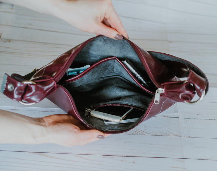 Open burgundy handbag on a light wooden surface#color_wine