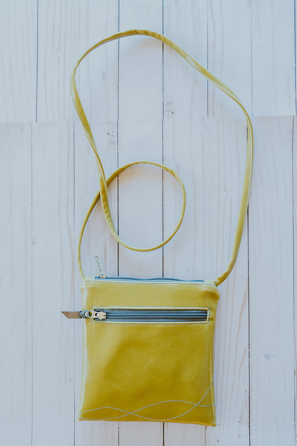 Yellow crossbody bag with a blue interior on a light wooden surface#color_lime-green-bloom