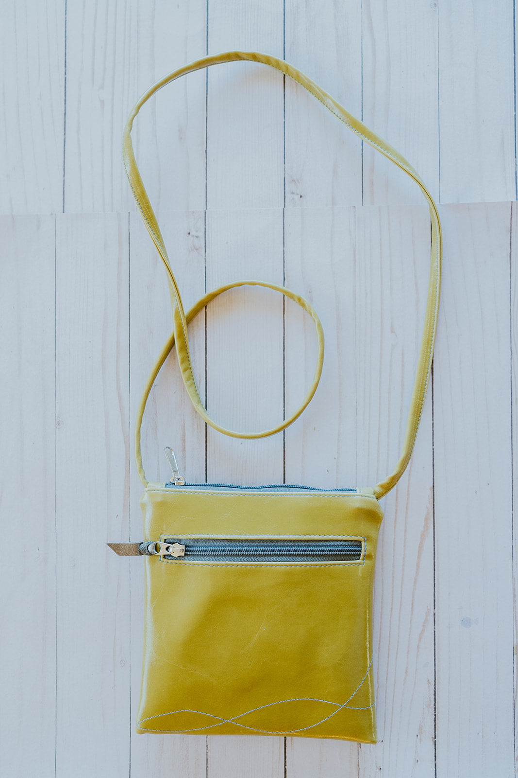 Yellow crossbody bag with a blue interior on a light wooden surface#color_lime-green-bloom