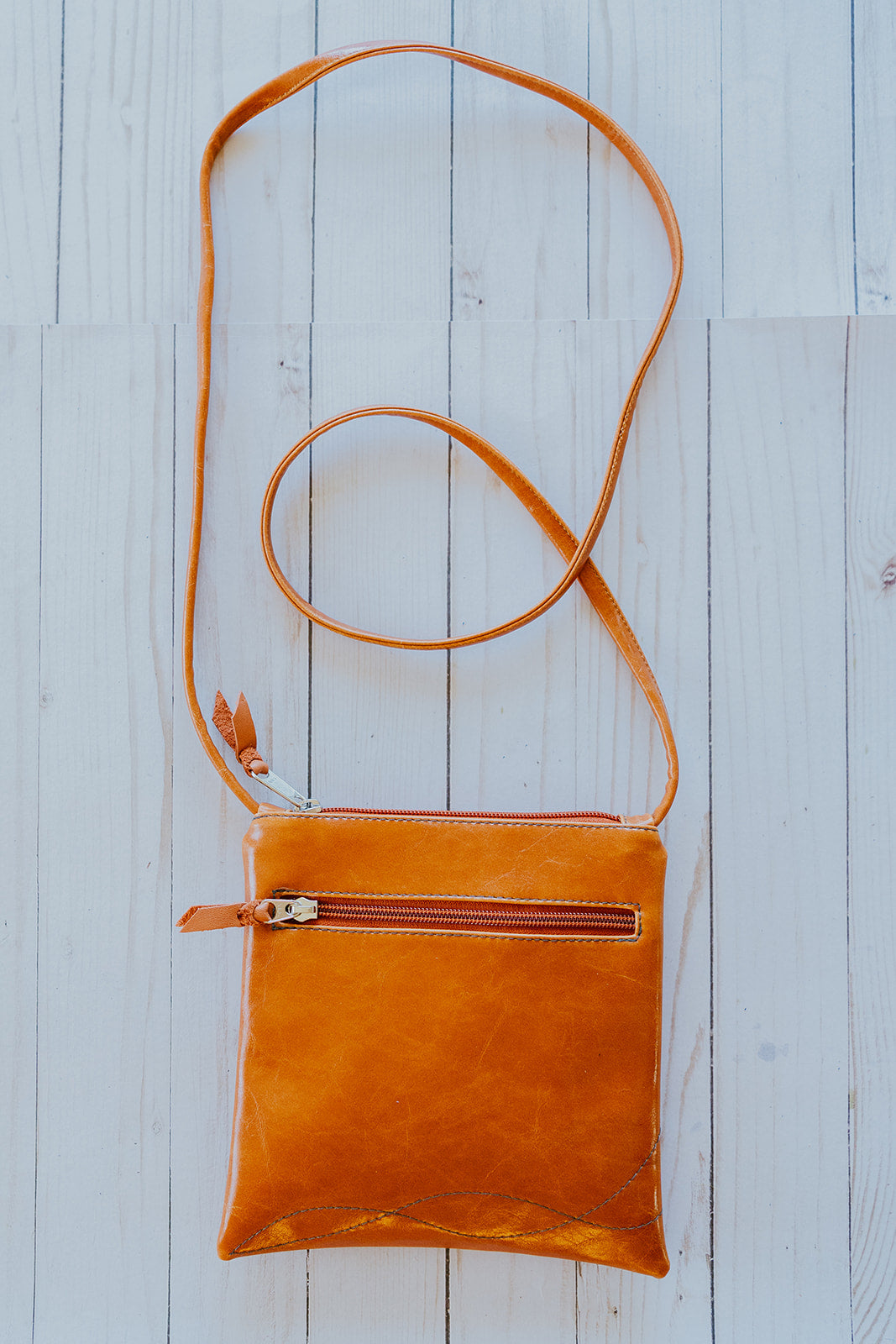 Orange leather crossbody bag on a light wooden surface#color_orange-bloom