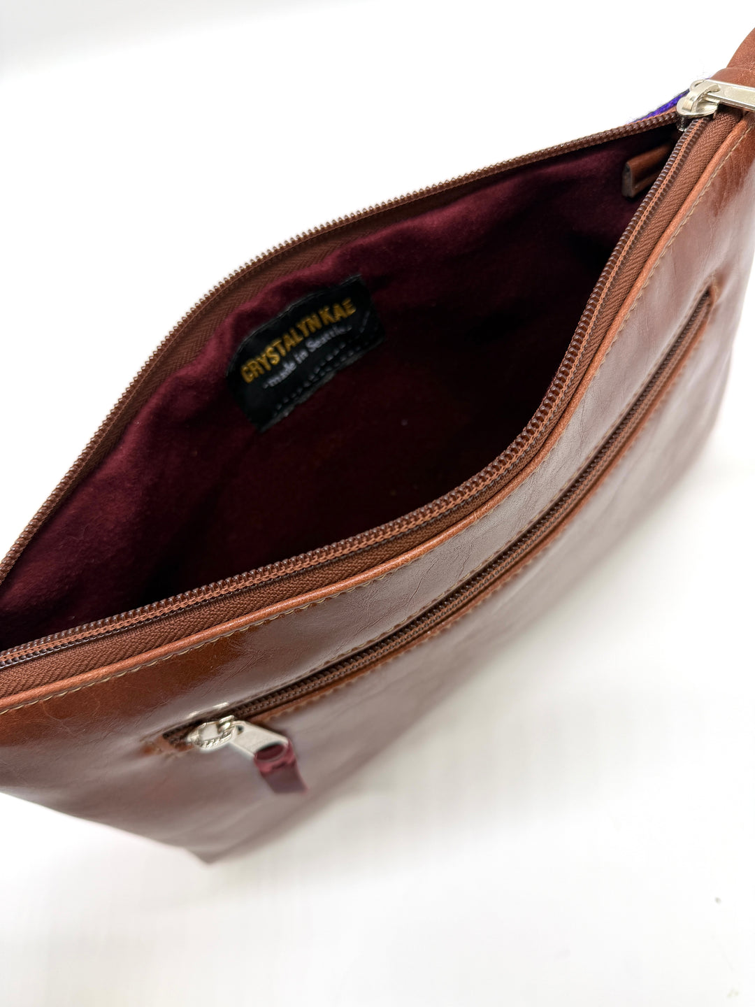 Brown leather bag with visible brand label on a white background#color_sky-arches-red-purple