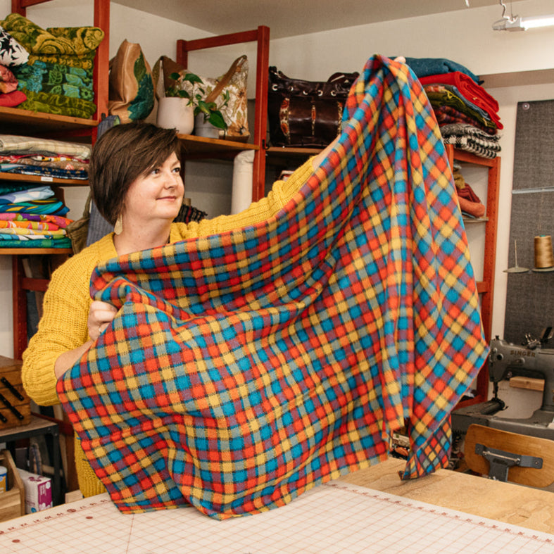 Person holding a colorful plaid fabric in a workshop setting