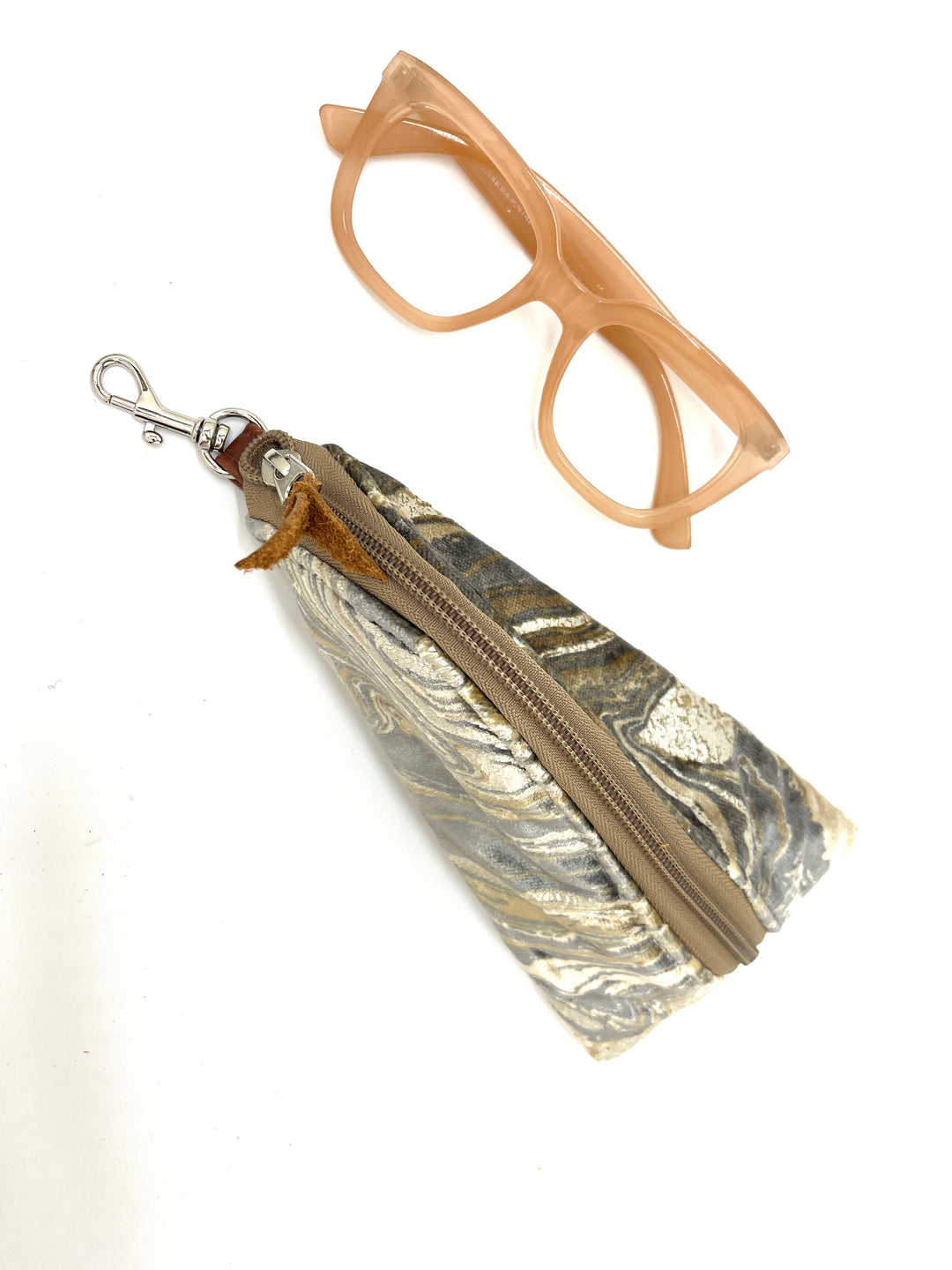 Marbled metallic pouch with zipper and beige cat-eye glasses on a white background#color_champagne-cosmos
