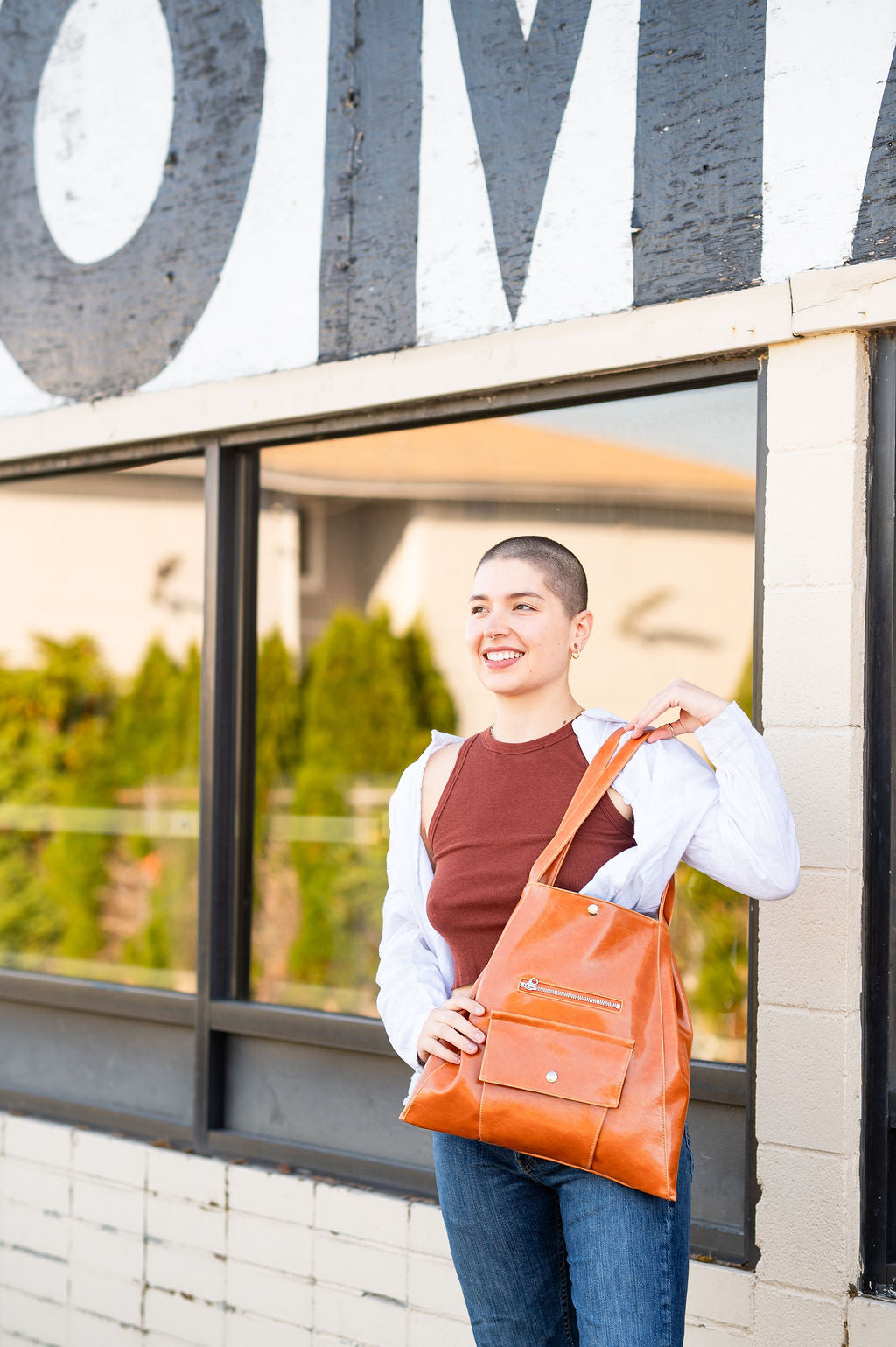 Woman holding an orange leather bag in front of a building with large letters.#color_butterscotch
