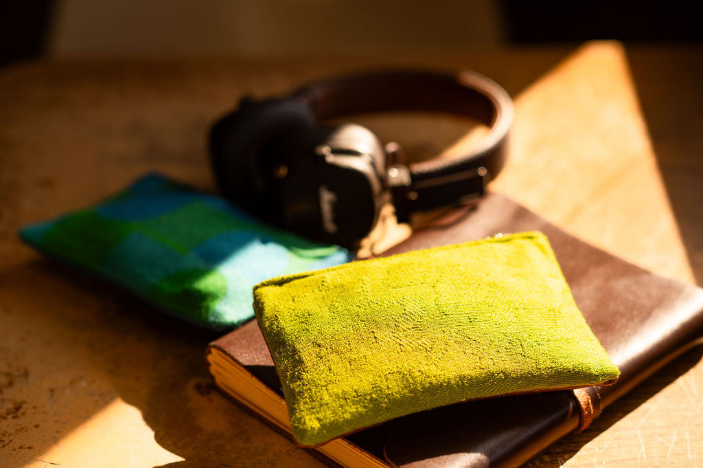 Green textured pouch on a notebook with headphones in the background#color_aerolinas-argentinas-green
