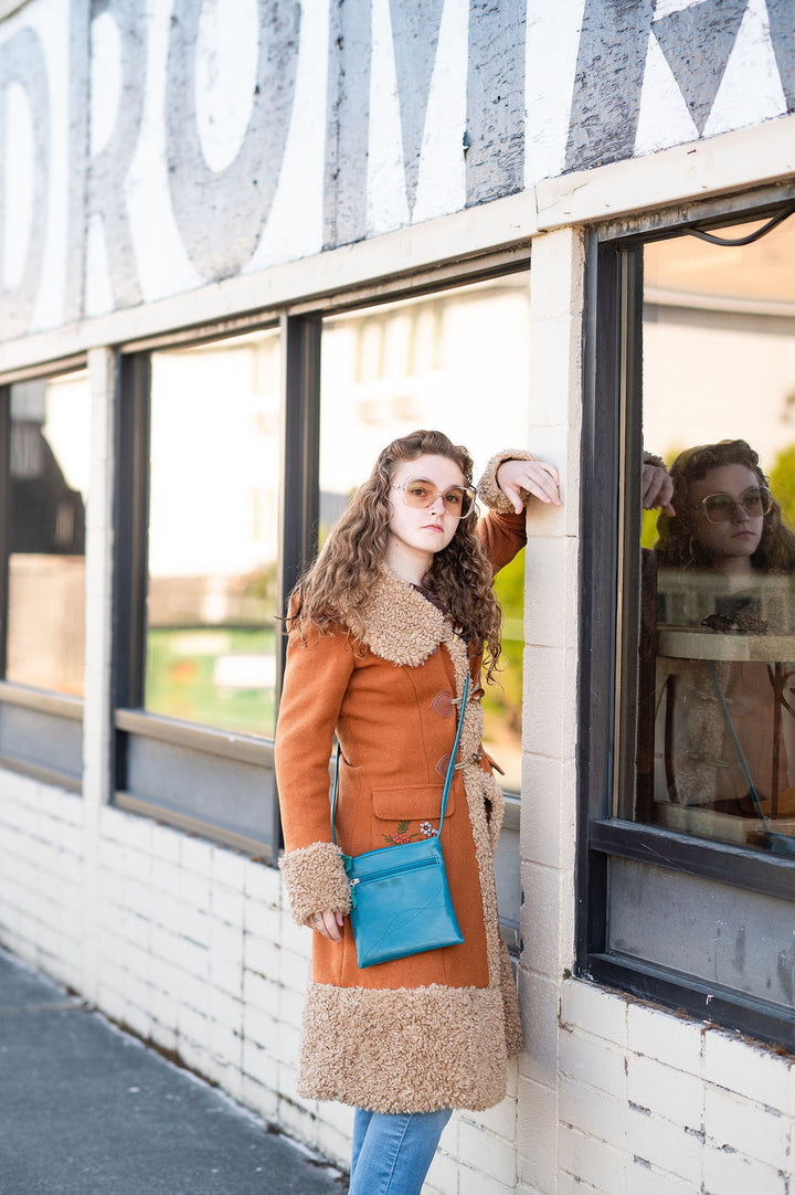 Woman in an orange coat with fur trim standing outside a laundromat
.#color_teal