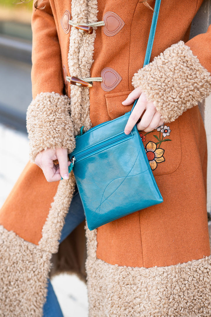 Person wearing an orange coat with a fluffy collar holding a blue purse.#color_teal