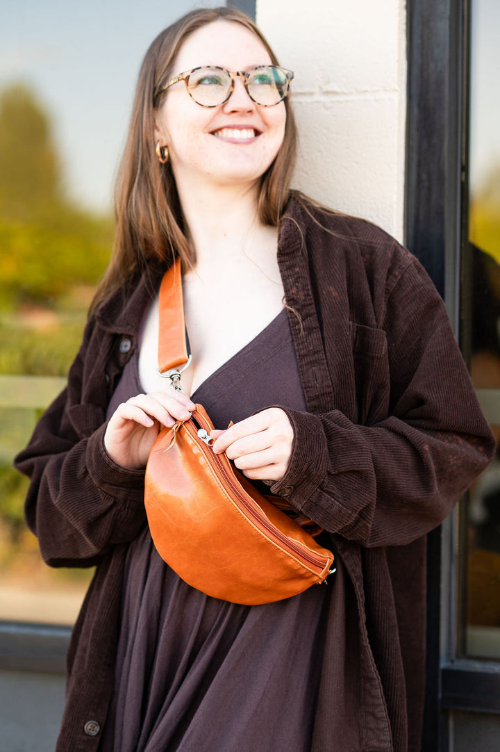 Woman holding a brown leather fanny pack bag outdoors#color_butterscotch