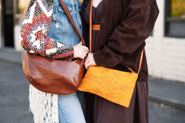 Two people holding leather bags on a street.#color_ale-brown