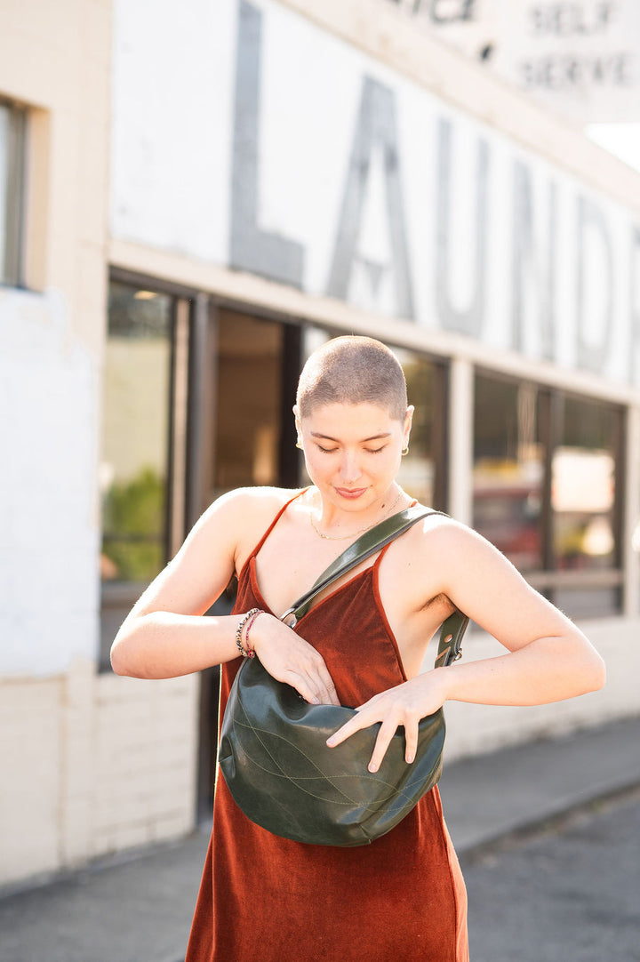 Woman in a red dress holding a green bag outdoors with a building in the background#color_emerald-green