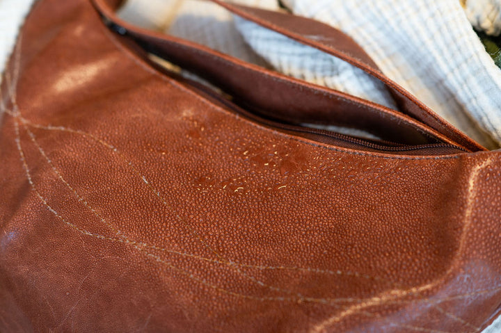 Close-up of a brown leather bag with a zipper, showing water droplets#color_ale-brown