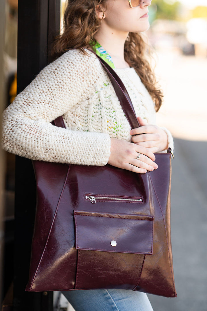 Person holding a brown leather tote bag outdoors#color_wine