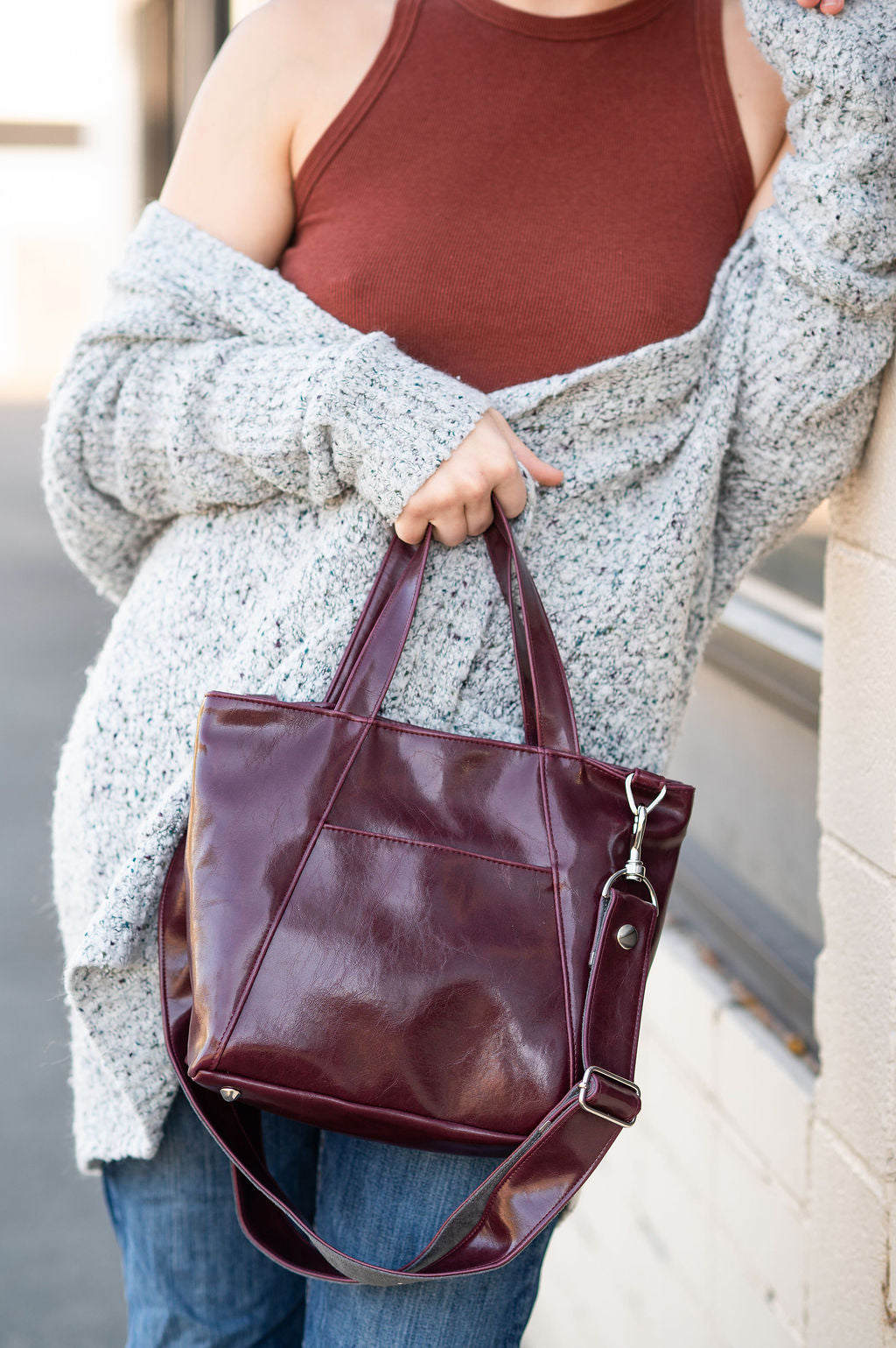 Person holding a maroon handbag with a neutral background#color_wine