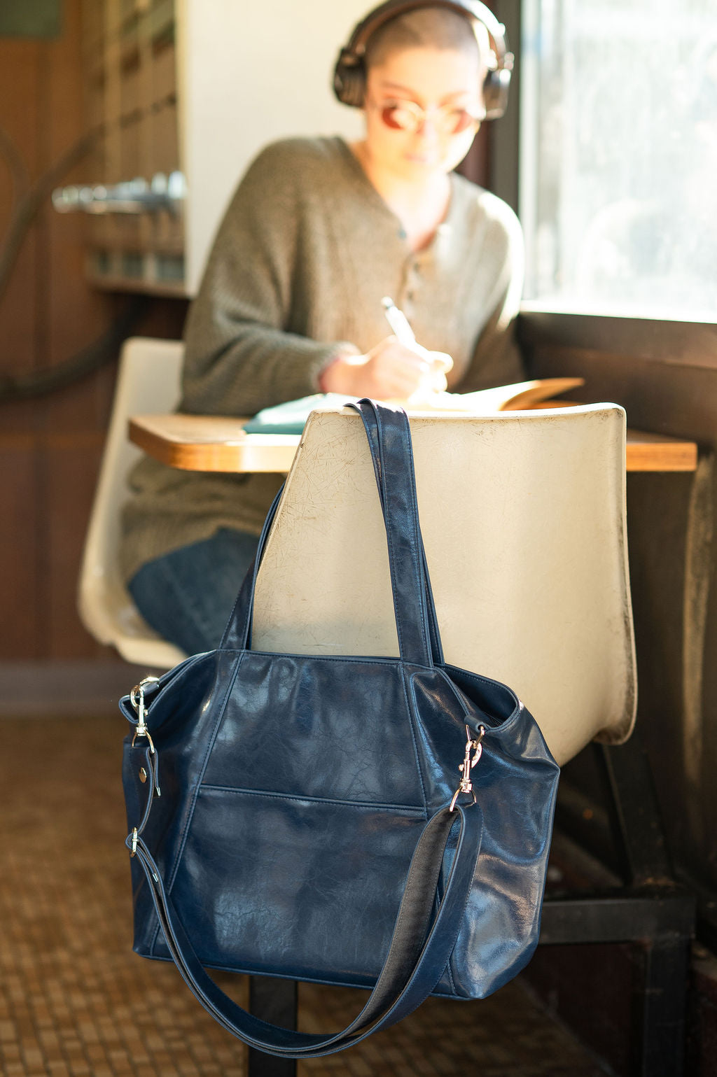 Blue handbag on a chair with a person studying in the background#color_navy