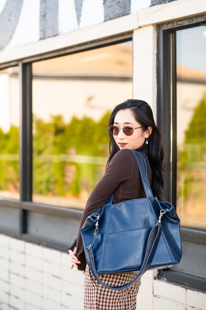 Woman holding a blue work tote for laptops outdoors near a building with large windows.#color_navy