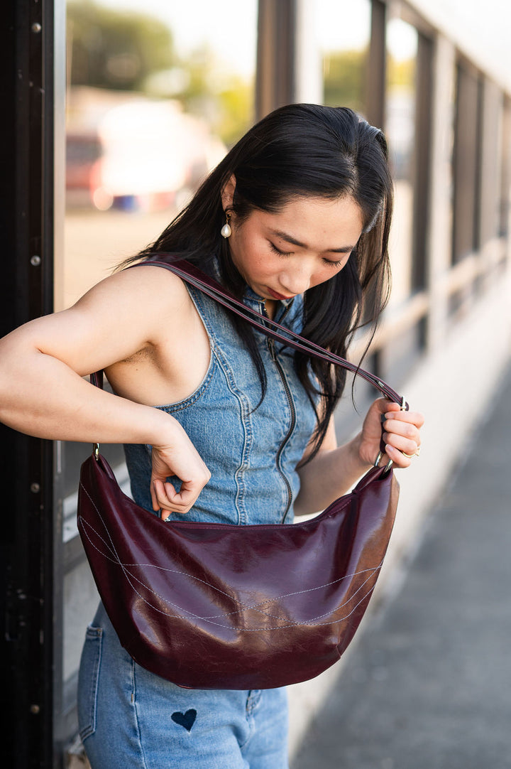 Woman holding a burgundy leather handbag outdoors#color_wine