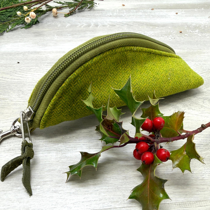 Green fabric pouch with a zipper on a light wooden surface with holly leaves and berries.