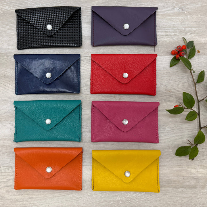 Set of colorful leather card holders on a light wooden surface with decorative branches.