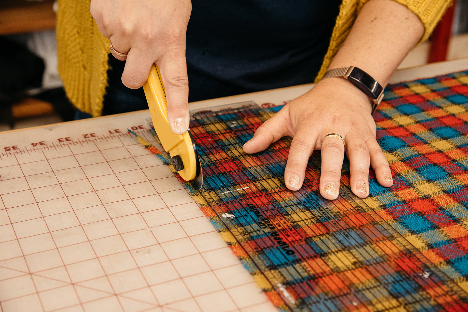 Person cutting a colorful woven fabric with a yellow tool on a grid surface.